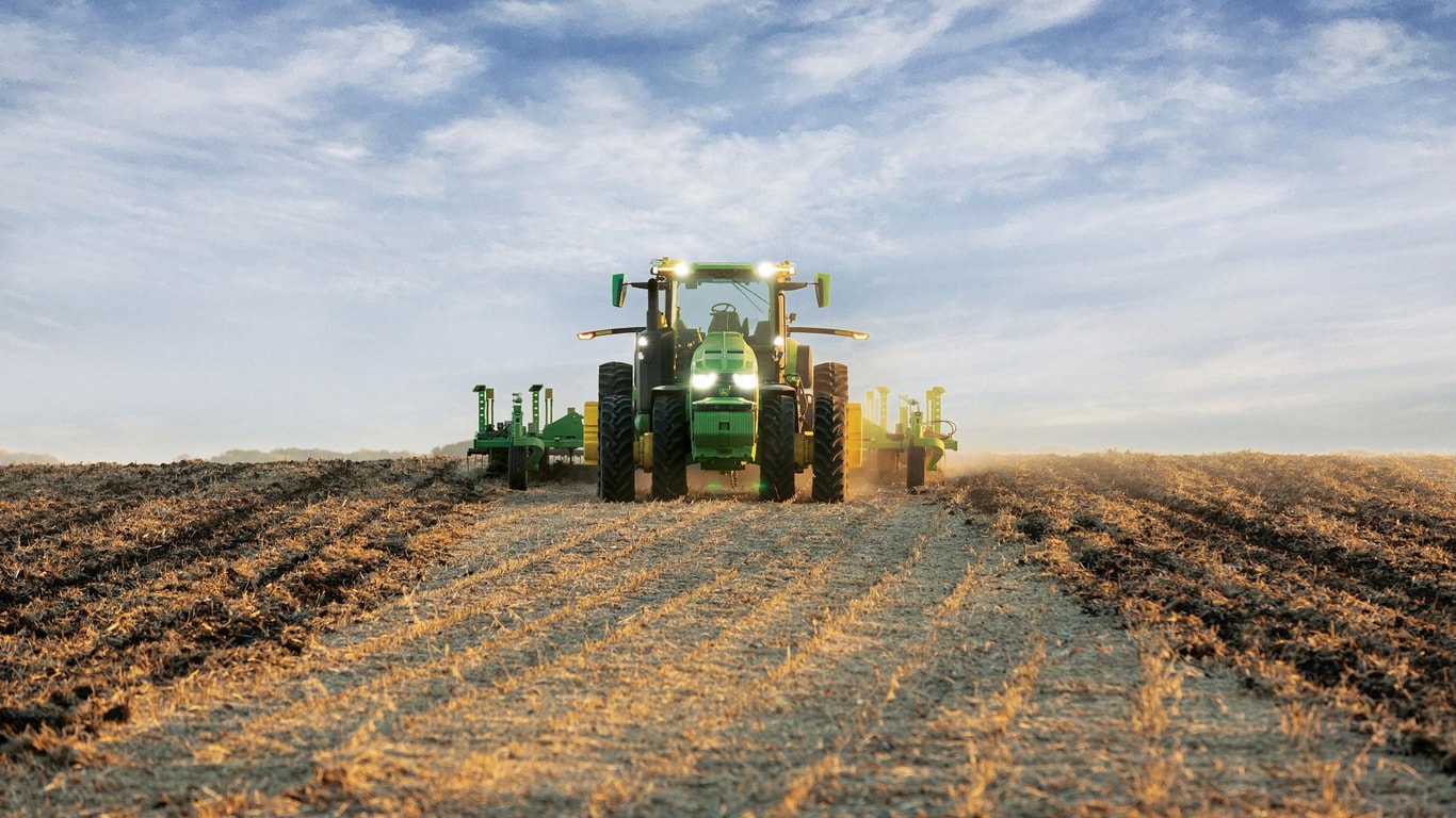 Samovozni traktor John Deere vleče opremo za oranje po odprtem polju.