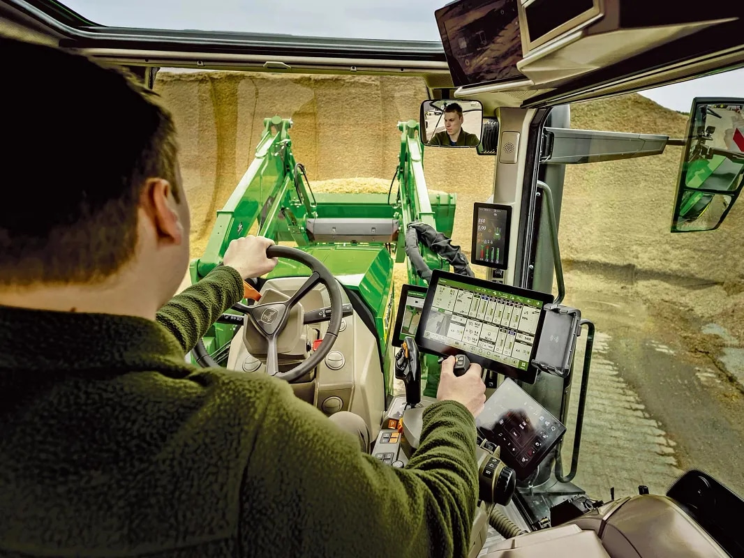 Prikaz notranjosti kabine traktorja John Deere prikazuje upravljalne elemente in delovanje sprednjega nakladalnika.