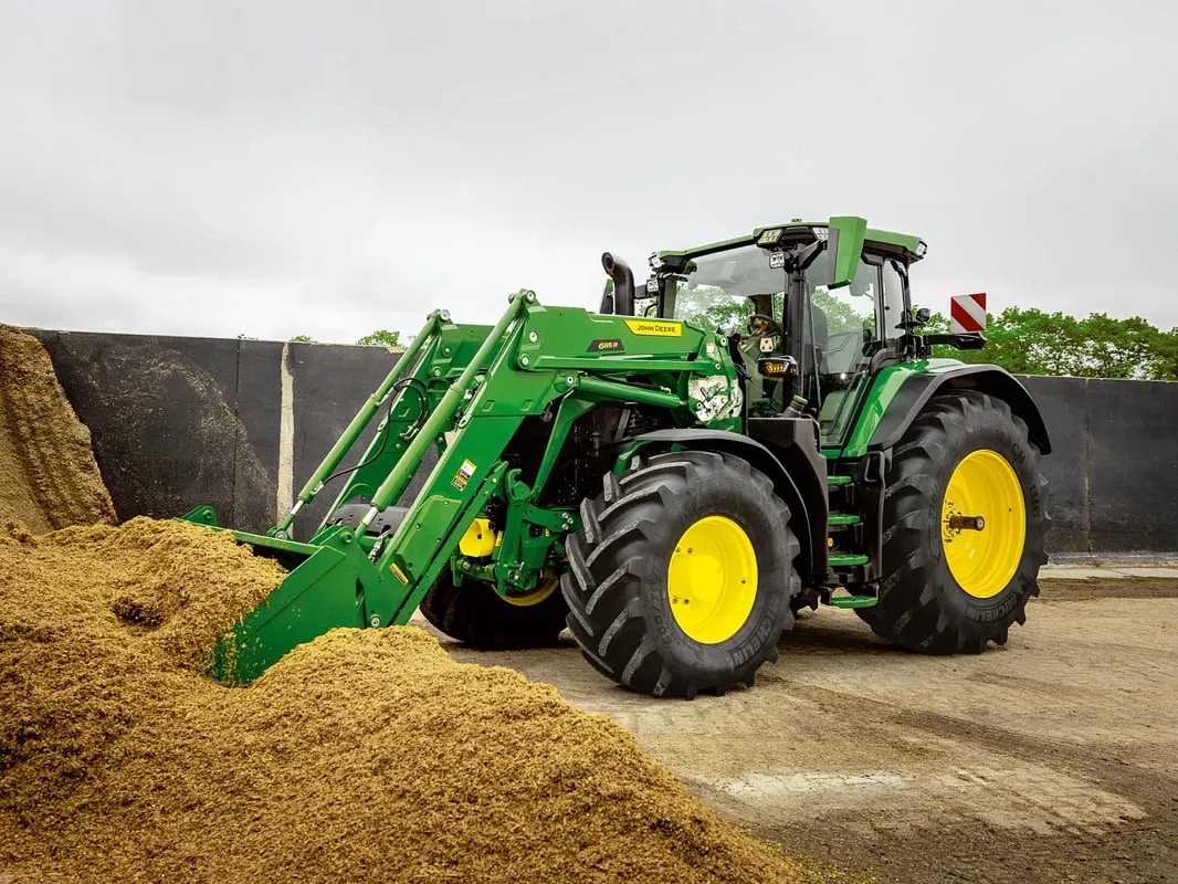 Traktor John Deere potiska kup silaže z žlico sprednjega nakladalnika na kmetiji.