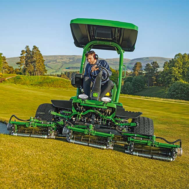 Vzdrževalec zelenic kosi na travnatem območju s kosilnico za green John Deere pri pogledu od spredaj.