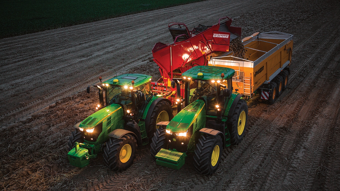 Traktor, ki vleče stroj za pobiranje krompirja raztovarja krompir v prikolico, ki jo vleče drug traktor