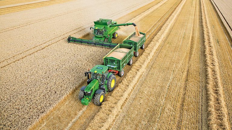 Kombajn John Deere serije S raztovarja p&scaron;enico v dve prikolici, ki ju vleče traktor