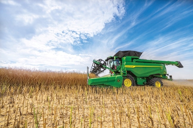 Kombajn John Deere za žetev zrnja z glavo na polju pod modrim nebom med žetvijo poljščine