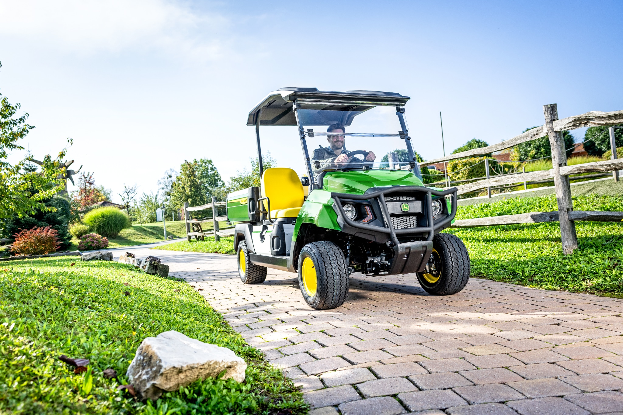 Večnamensko vozilo Gator GS vozi po tlakovani poti v urejenem okolju Večnamensko vozilo Gator GS vozi po tlakovani poti v urejenem okolju