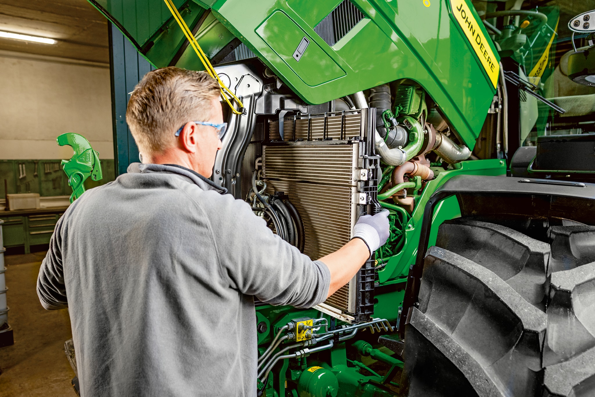 Serviser izvaja vzdrževalna dela na motorju traktorja serije John Deere 6M.