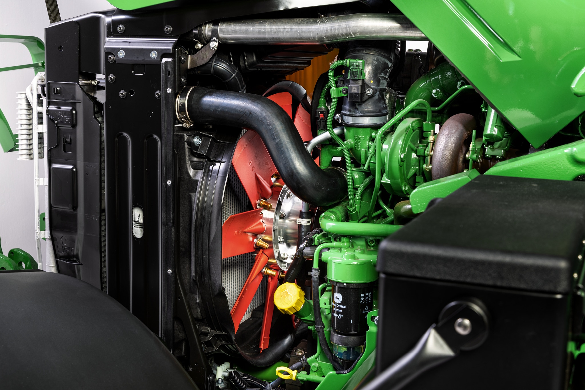 Pogled od blizu na motorni prostor traktorja John Deere serije 6M, ki poudarja hladilni sistem in komponente motorja.