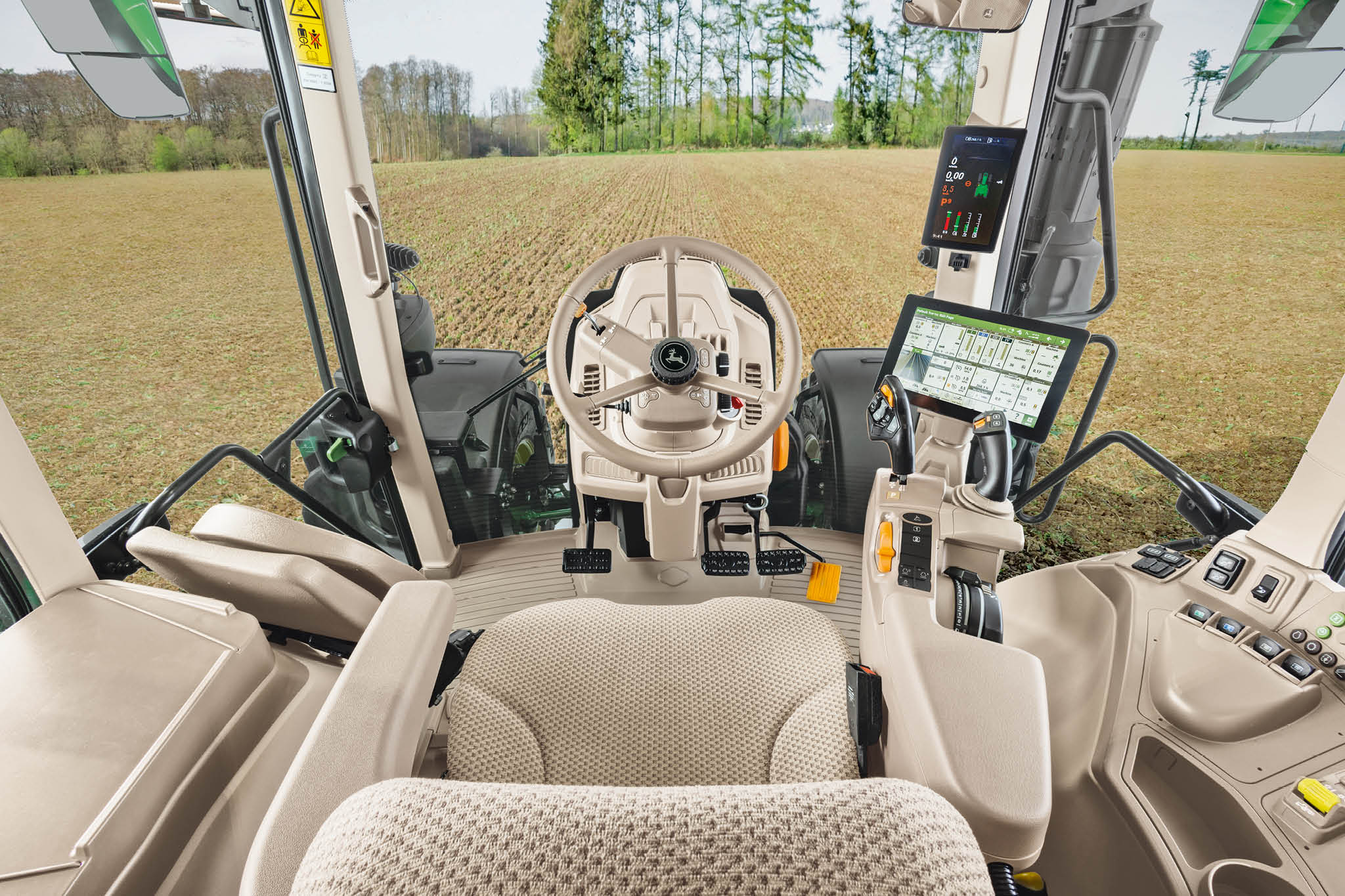 Notranji pregled kabine traktorja John Deere serije 6M z voznikovim sedežem, volanom in digitalnimi prikazovalniki.