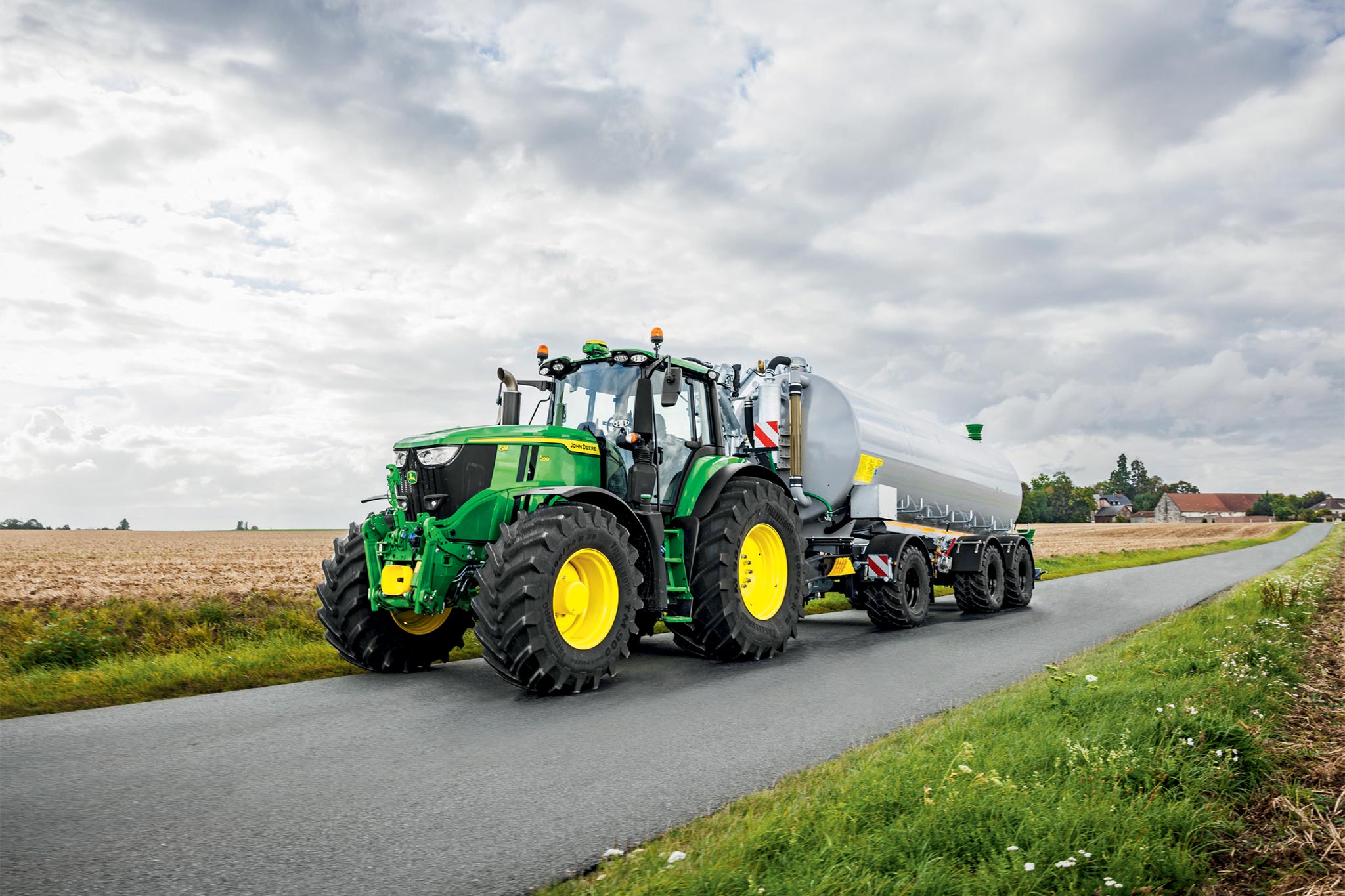 Traktor John Deere serije 6M obdeluje požeto polje s širokimi kultivatorji, gledano od zgoraj, ko se dviga prah.
