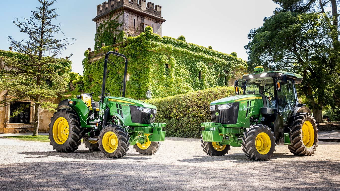 S soncem obsijan zeleno-rumeni traktor John Deere 5075EN vozi po poti skozi sadovnjak.