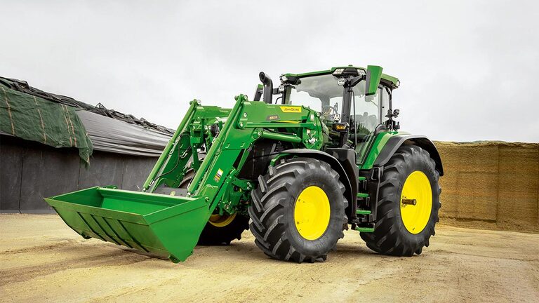 Traktor John Deere s sprednjim nakladalnikom, parkiran na dvorišču v bližini skladišča silaže.