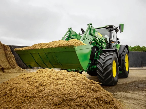 Traktor John Deere s sprednjim nakladalnikom prevaža razrezano silažo v kmetijsko skladišče.