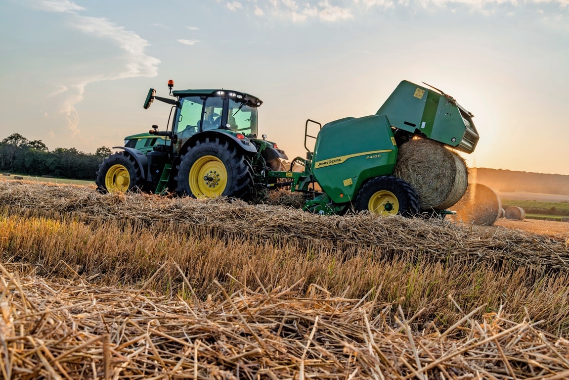 Traktor John Deere 6M vleče balirko John Deere F442M, ki izvrže balo za travo