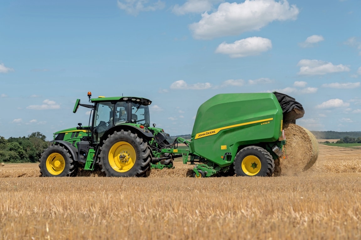 Traktor John Deere 6R 150 na polju za slamo vleče balirko John Deere V452R, ki izvrže balo
