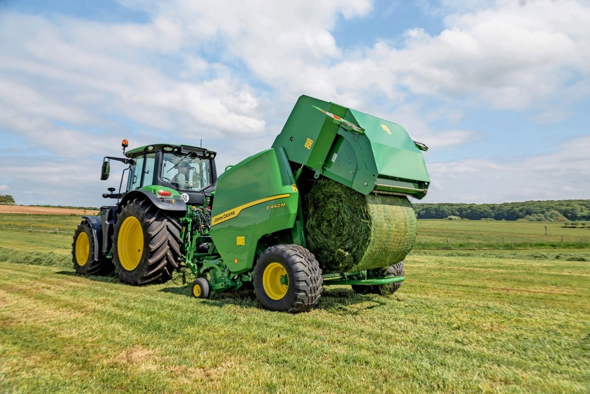 Traktor John Deere 6M vleče balirko John Deere F442M, ki izvrže balo za travo
