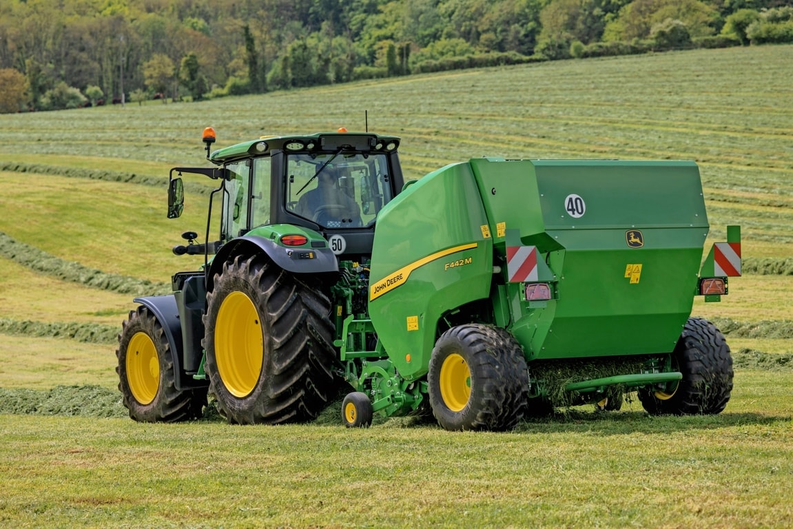 Traktor John Deere 6M na hribovitem travnatem polju vleče balirko John Deere F442M