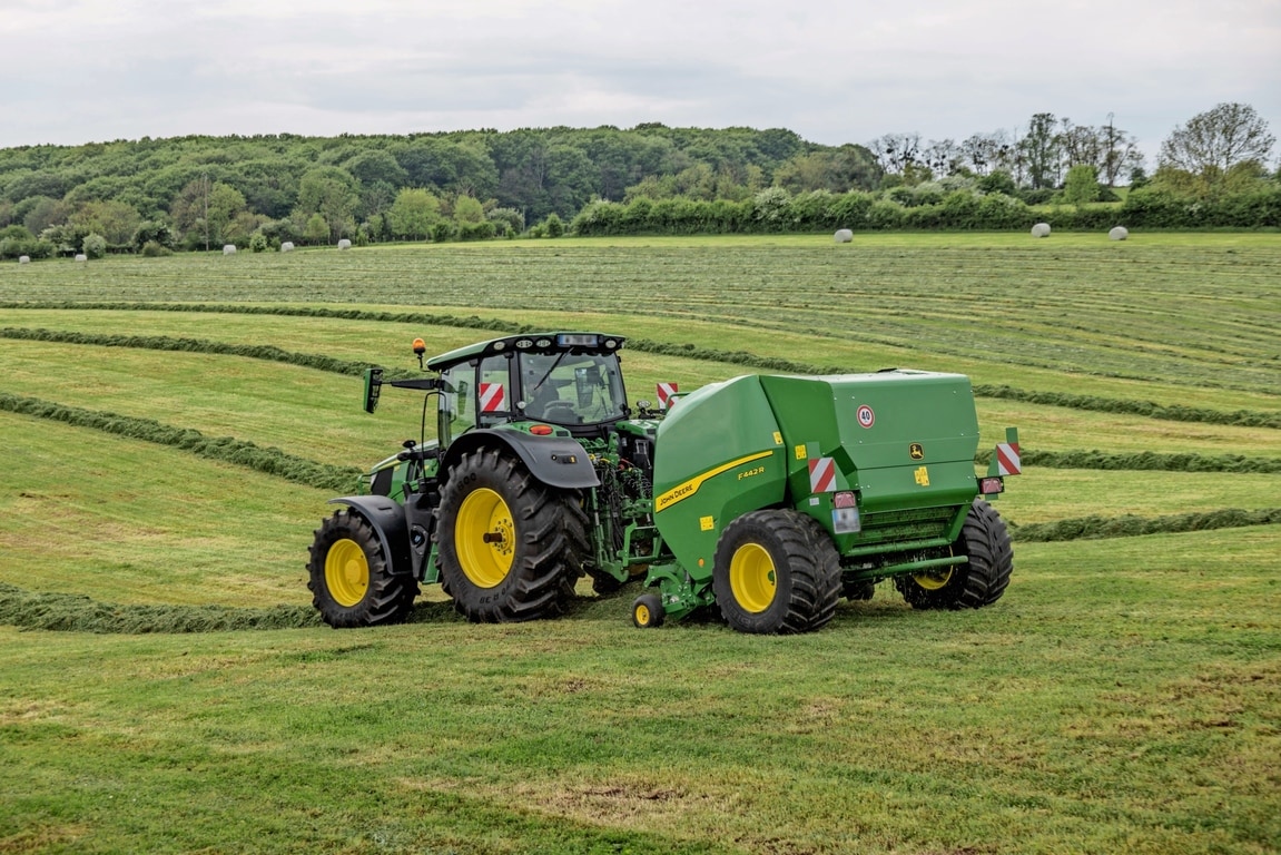 Traktor John Deere 6M na hribovitem travnatem polju vleče balirko John Deere F442M